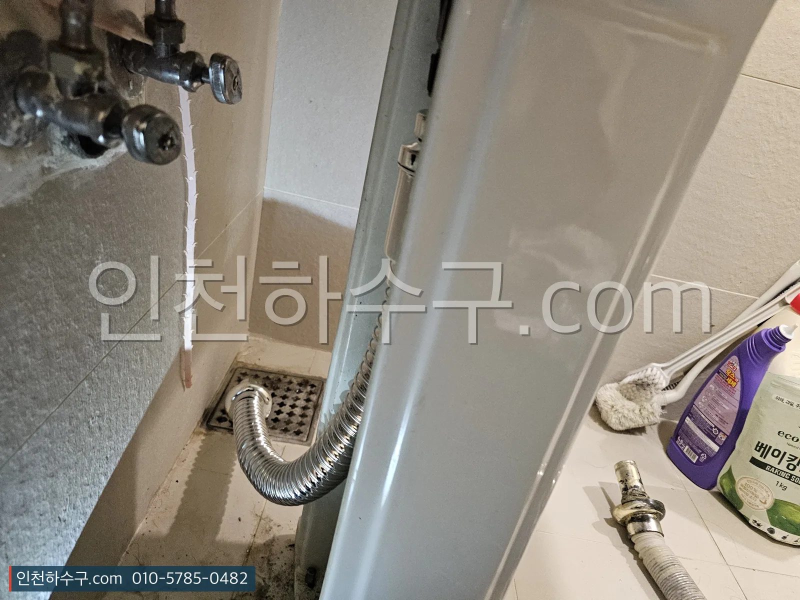 삭은 주름 배수관이 바닥 배수구로 이어져 있는 세면대 아래 모습